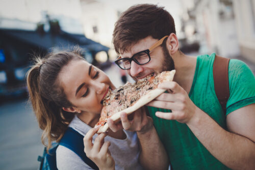 Happy couple sharing pizza on street