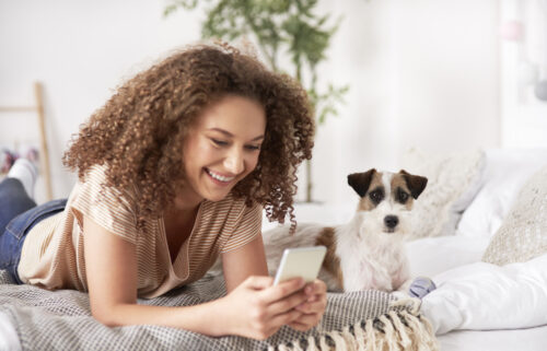 Young woman and dog on bed looking at phone