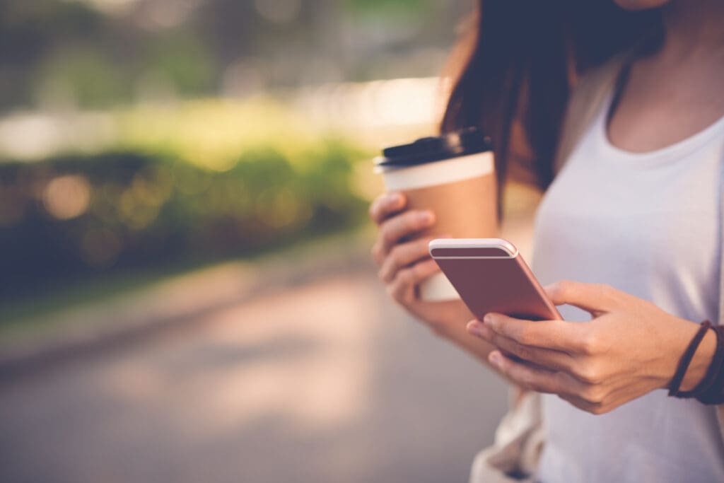 Close-up image of woman texting and drinking coffee outdoors